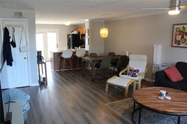 living room with dark wood-type flooring, ceiling fan, ornamental molding, and a textured ceiling