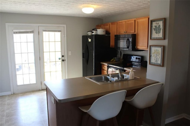 kitchen with sink, a kitchen breakfast bar, black appliances, a textured ceiling, and kitchen peninsula