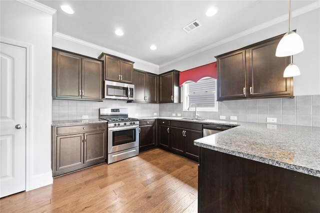 6535 Crosscreek Ln, Flowery Branch, GA 30542 - kitchen featuring appliances with stainless steel finishes, dark brown cabinets, light wood-type flooring, crown molding, and pendant lighting