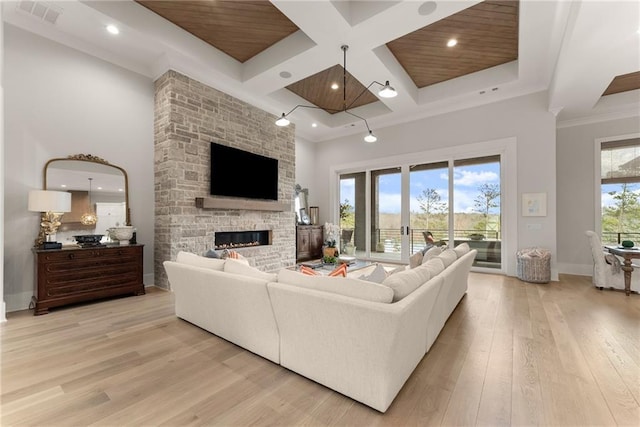 living area with light wood finished floors, visible vents, a stone fireplace, a high ceiling, and coffered ceiling