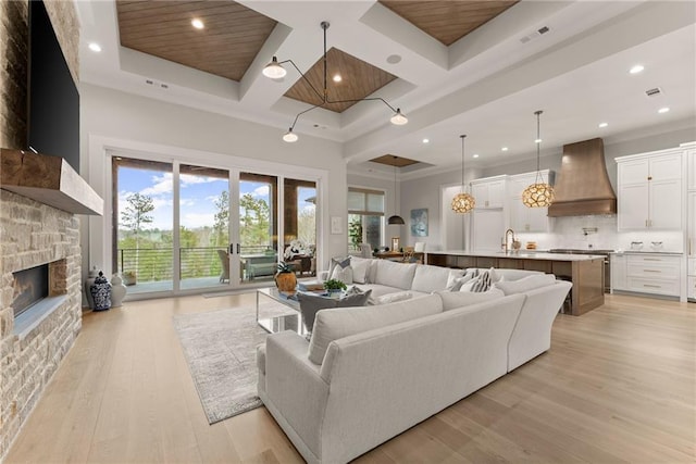 living area featuring visible vents, beam ceiling, coffered ceiling, a stone fireplace, and light wood finished floors