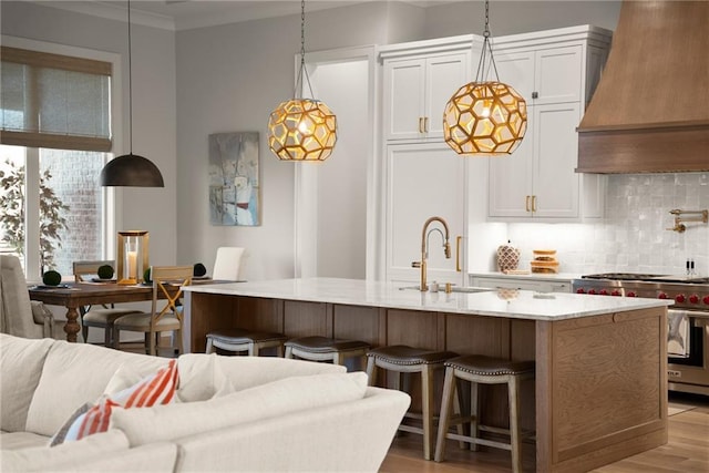 kitchen featuring backsplash, a center island with sink, custom range hood, premium range, and a sink