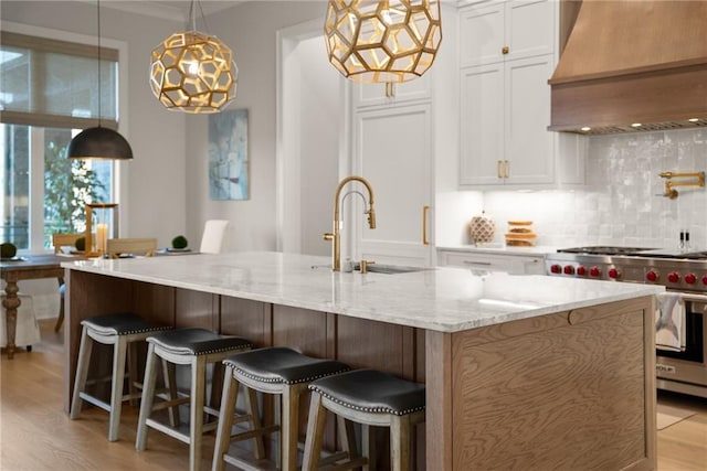 kitchen featuring premium range hood, tasteful backsplash, premium range, white cabinetry, and light wood-style floors