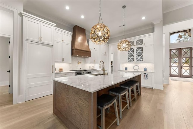 kitchen with premium range hood, light wood-type flooring, ornamental molding, and a sink