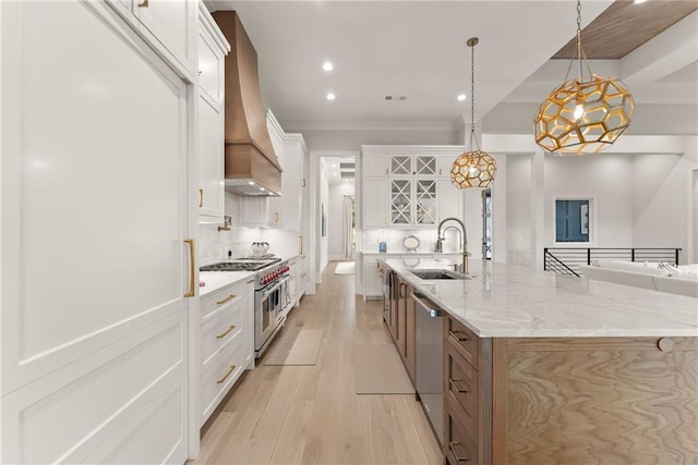 kitchen featuring a sink, decorative backsplash, custom range hood, appliances with stainless steel finishes, and light wood-type flooring