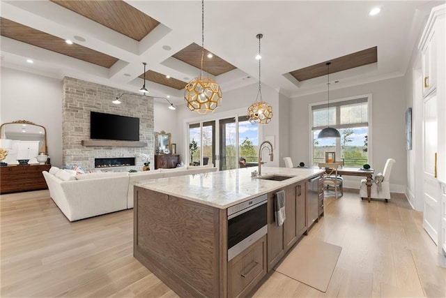 kitchen featuring a sink, light wood-type flooring, coffered ceiling, and a stone fireplace