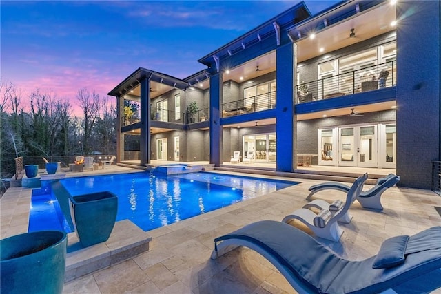 pool at dusk featuring a patio area, french doors, a pool with connected hot tub, and a ceiling fan