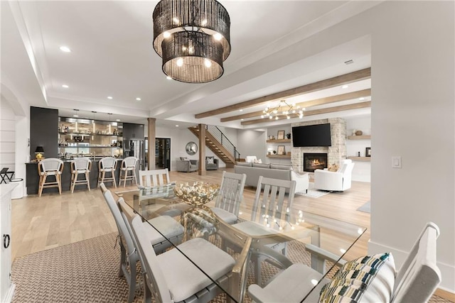 dining area featuring light wood finished floors, a large fireplace, beamed ceiling, recessed lighting, and a notable chandelier