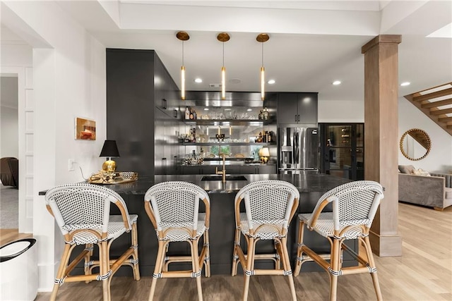 bar with decorative light fixtures, light wood-style flooring, wet bar, and stainless steel fridge with ice dispenser