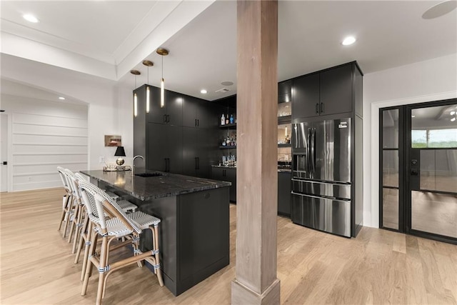 kitchen with a sink, a breakfast bar, fridge with ice dispenser, light wood-style flooring, and dark cabinets