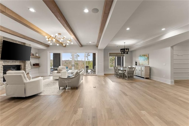 living area featuring light wood finished floors, baseboards, a chandelier, beamed ceiling, and a fireplace