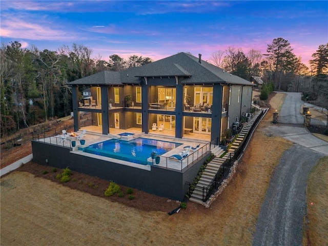 back of house at dusk featuring a patio area, a shingled roof, a balcony, and fence