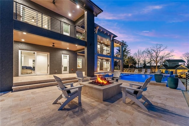 patio terrace at dusk featuring a balcony, a fenced in pool, and an outdoor fire pit