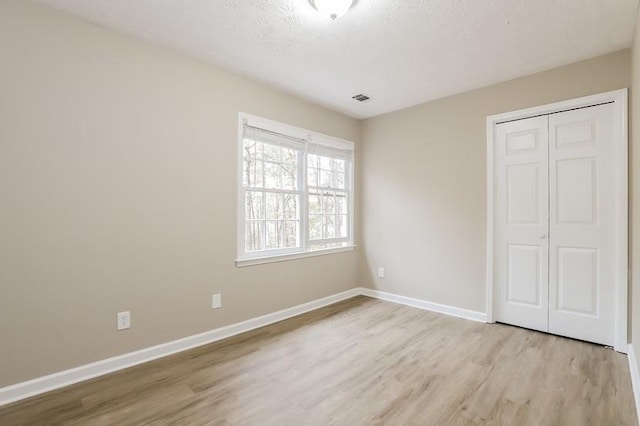 unfurnished bedroom with a textured ceiling, light wood-type flooring, and a closet