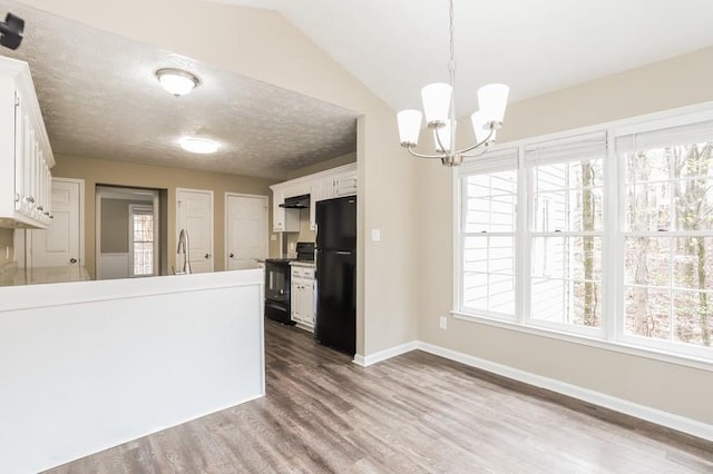 kitchen with dark wood-type flooring, black refrigerator, range with electric cooktop, white cabinets, and decorative light fixtures