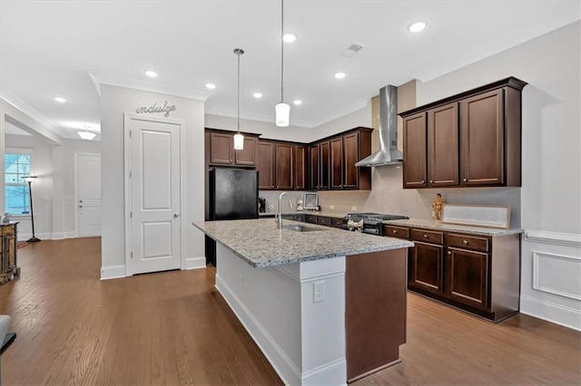 kitchen with sink, decorative light fixtures, an island with sink, light stone countertops, and wall chimney range hood