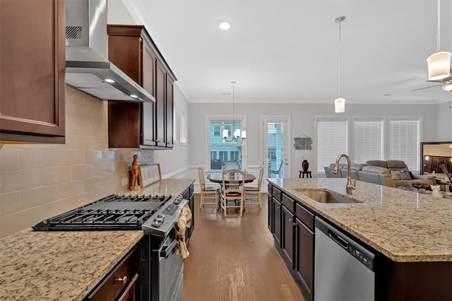 kitchen with stainless steel appliances, pendant lighting, sink, and wall chimney range hood