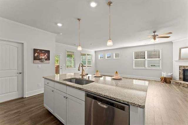 kitchen with ornamental molding, light stone counters, a stone fireplace, stainless steel dishwasher, and a sink