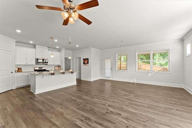 kitchen with stainless steel appliances, open floor plan, white cabinets, a kitchen island with sink, and wood finished floors