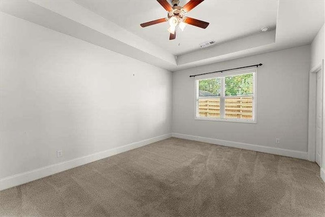 empty room featuring light colored carpet, a tray ceiling, visible vents, and baseboards