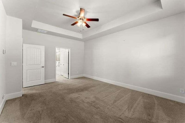 carpeted spare room with baseboards, a tray ceiling, and a ceiling fan