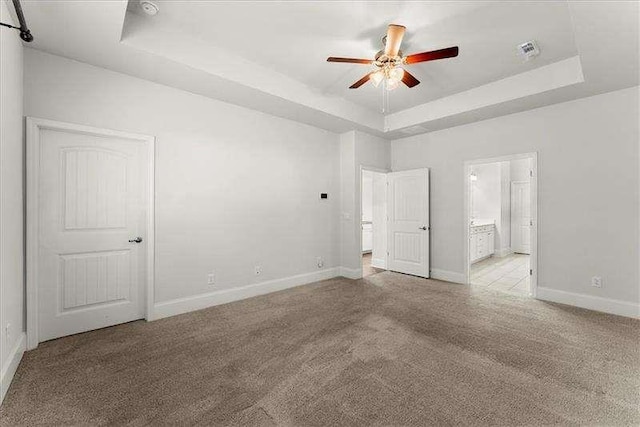 unfurnished bedroom with light colored carpet, a tray ceiling, visible vents, and baseboards