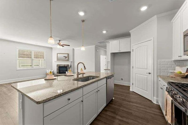 kitchen featuring a fireplace, a sink, white cabinets, open floor plan, and appliances with stainless steel finishes