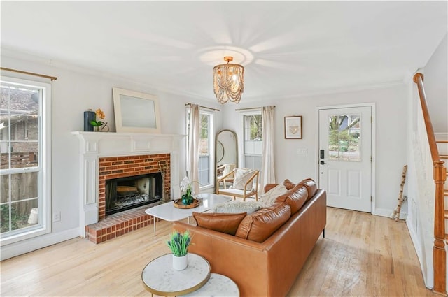 living room featuring baseboards, ornamental molding, stairway, a brick fireplace, and light wood finished floors