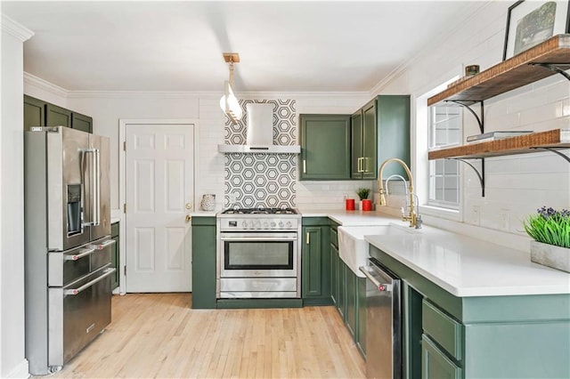 kitchen featuring stainless steel appliances, green cabinetry, a sink, and wall chimney exhaust hood