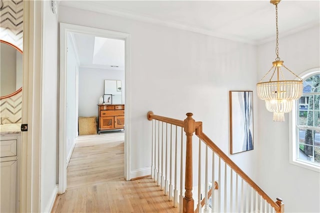 corridor featuring ornamental molding, light wood-style flooring, an upstairs landing, and a notable chandelier