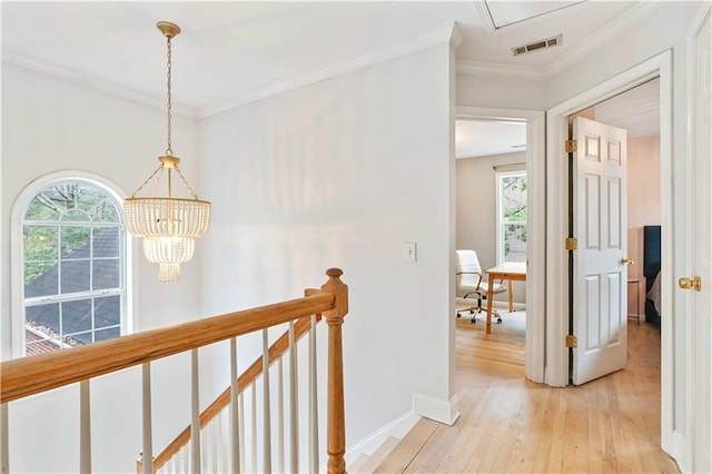 hallway featuring light wood finished floors, baseboards, visible vents, crown molding, and an upstairs landing