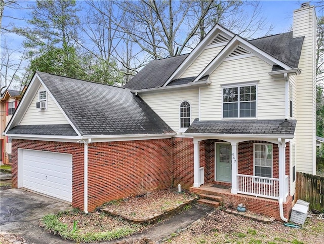 traditional home featuring brick siding, a chimney, covered porch, an attached garage, and driveway