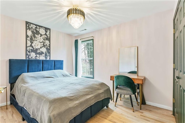 bedroom featuring a notable chandelier, wood finished floors, visible vents, and baseboards