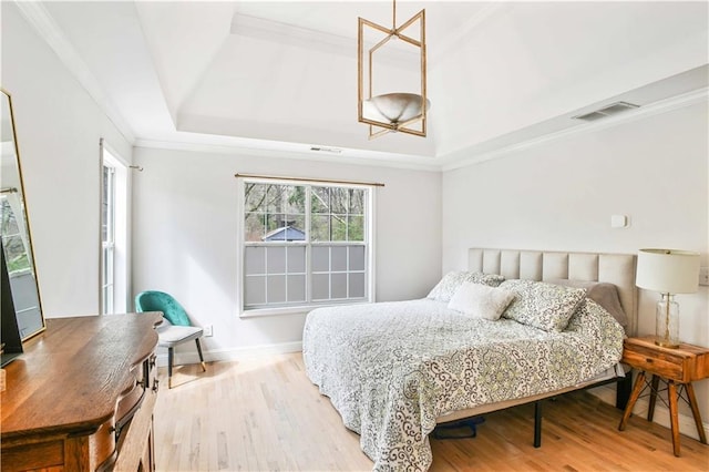 bedroom with wood finished floors, ornamental molding, a raised ceiling, and visible vents