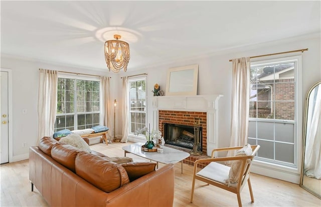 living room with a chandelier, light wood-type flooring, a brick fireplace, and plenty of natural light