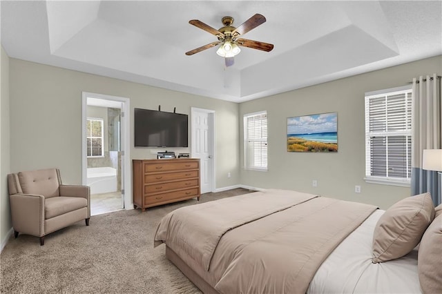 carpeted bedroom with ceiling fan, ensuite bath, and a tray ceiling