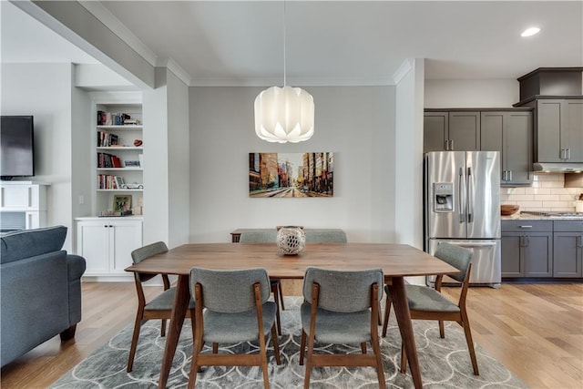 dining space featuring built in shelves, ornamental molding, and light hardwood / wood-style floors