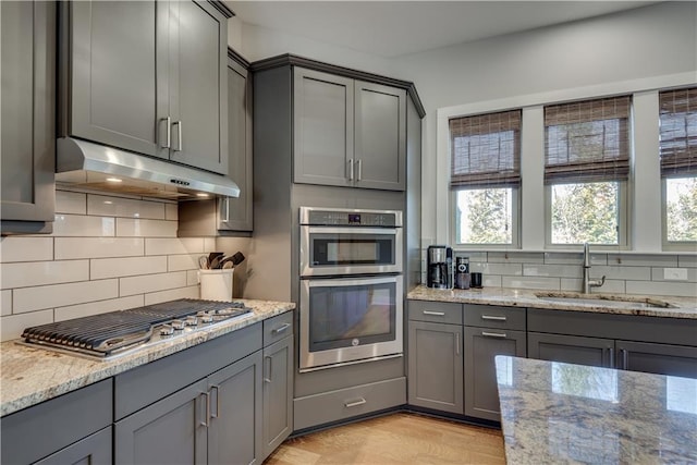 kitchen with gray cabinetry, sink, light stone countertops, and appliances with stainless steel finishes