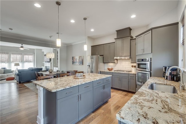 kitchen with sink, stainless steel appliances, hanging light fixtures, and light stone countertops