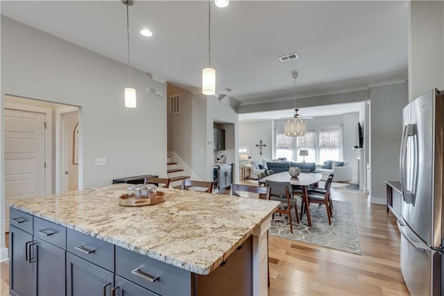 kitchen with light stone counters, hanging light fixtures, stainless steel fridge, a kitchen island, and light hardwood / wood-style floors