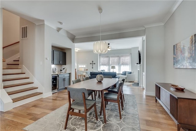 dining space with ornamental molding, beverage cooler, and light hardwood / wood-style floors