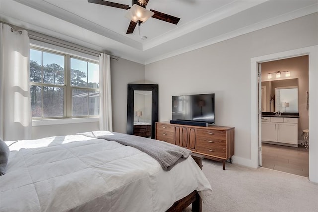 bedroom with connected bathroom, light carpet, ornamental molding, a tray ceiling, and ceiling fan