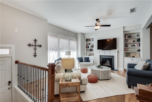 living room with built in shelves, ceiling fan, and hardwood / wood-style flooring