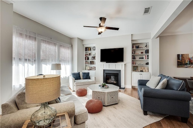 living room with built in shelves, ceiling fan, and wood-type flooring