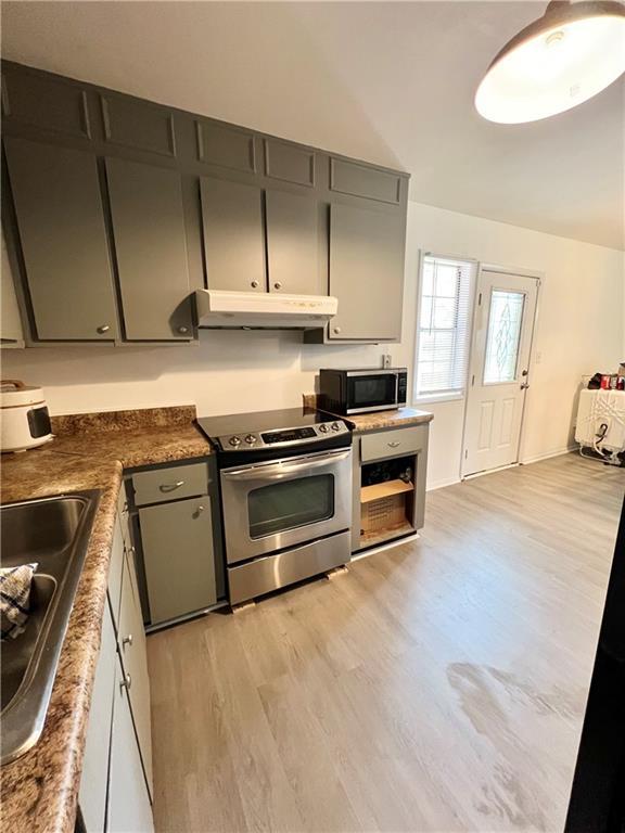 kitchen with dark countertops, under cabinet range hood, a sink, light wood-type flooring, and electric range