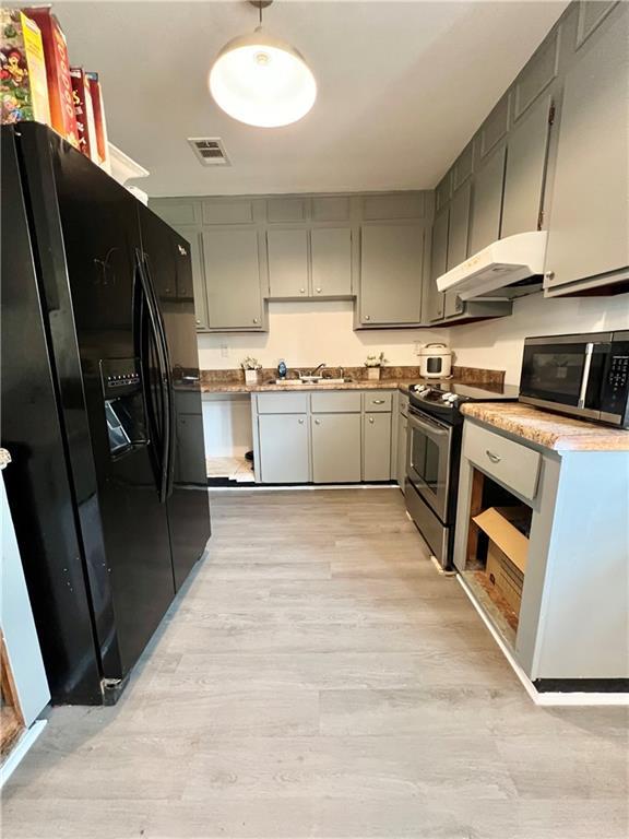 kitchen with a sink, appliances with stainless steel finishes, light wood-type flooring, under cabinet range hood, and visible vents