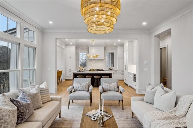 living room with crown molding, sink, light hardwood / wood-style flooring, and a notable chandelier