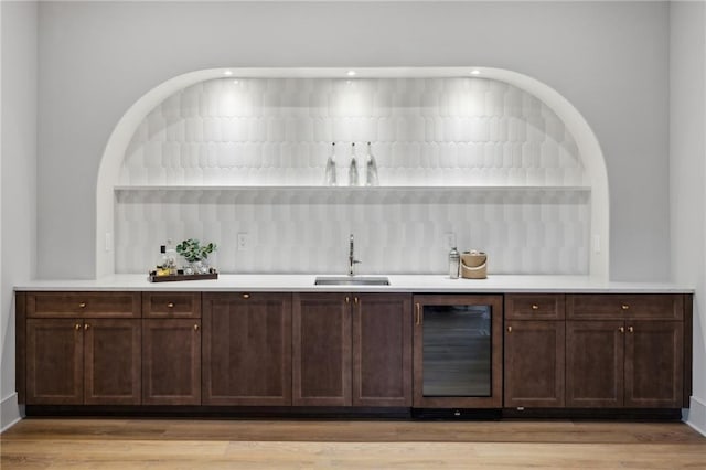 bar featuring sink, dark brown cabinets, light hardwood / wood-style floors, and beverage cooler