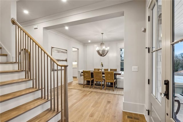 entryway with ornamental molding, an inviting chandelier, and light hardwood / wood-style floors