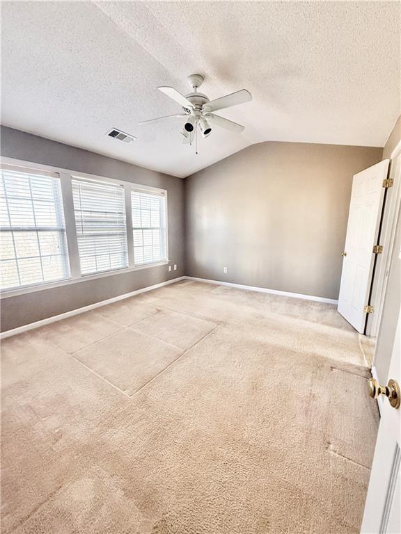 carpeted empty room with lofted ceiling, a textured ceiling, visible vents, baseboards, and a ceiling fan